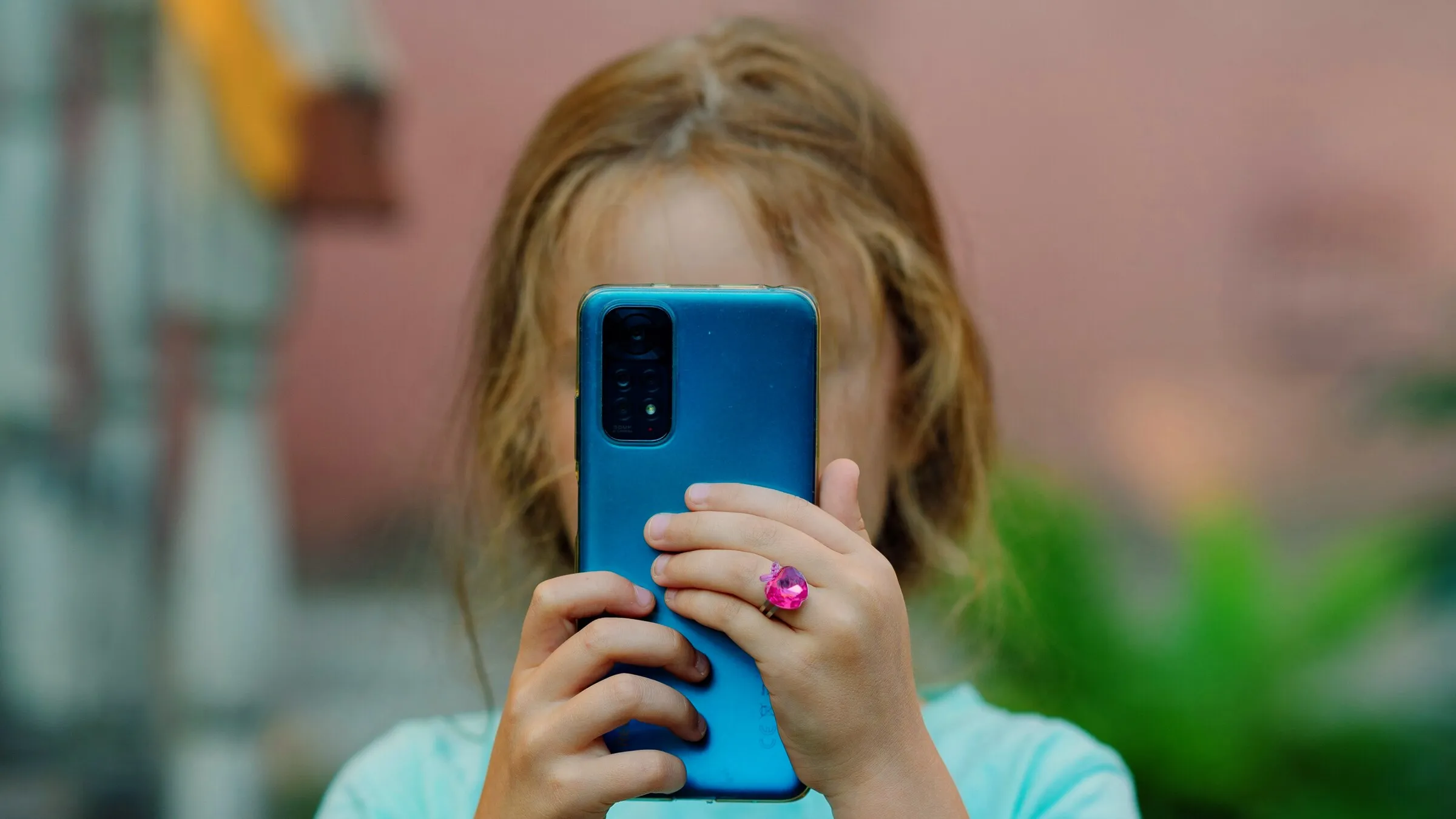 A child holds a phone in front of their face, its camera pointing back at the viewer, in warm light.