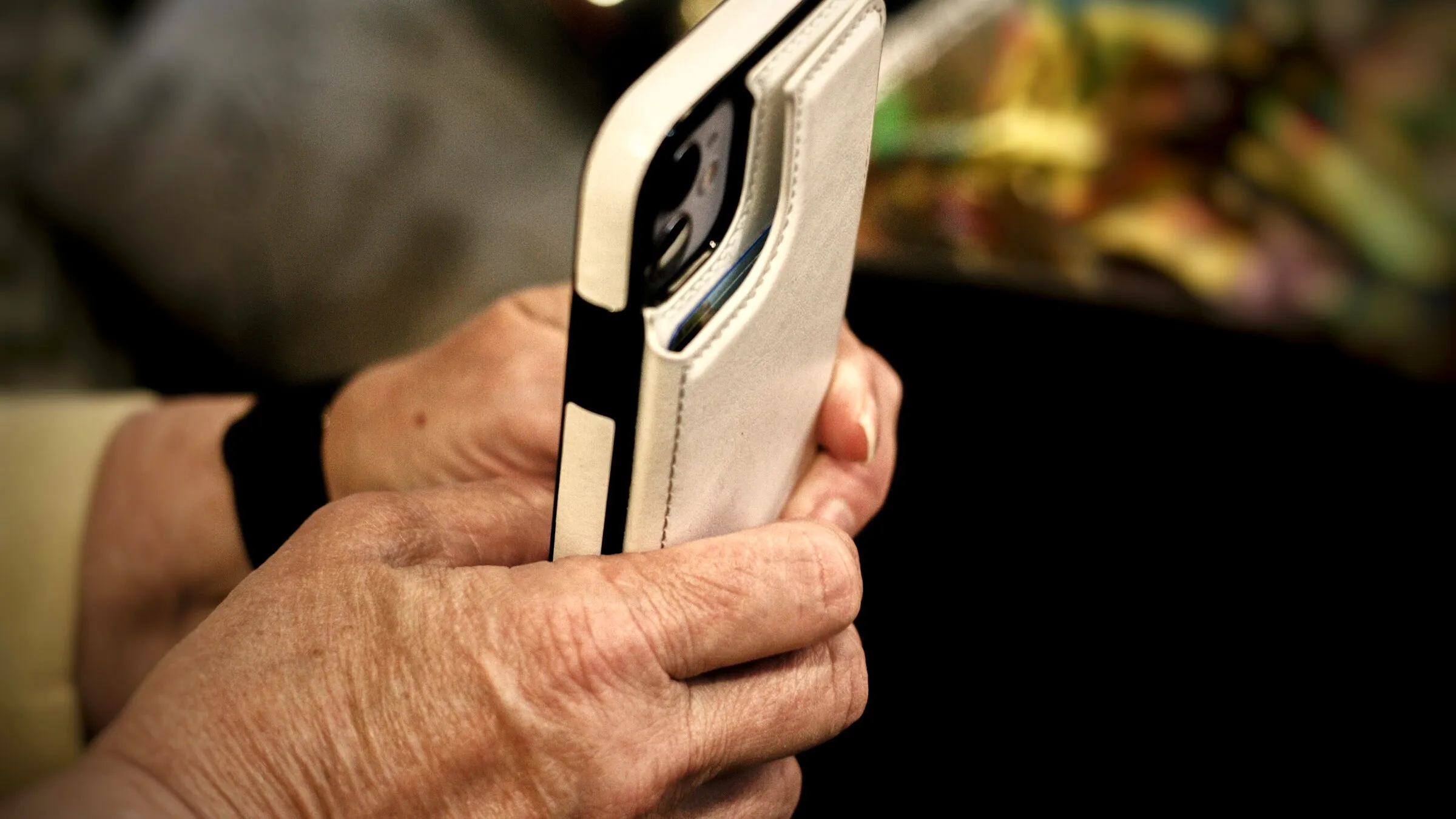 An older person's hands holding a phone, close up, in warm light.