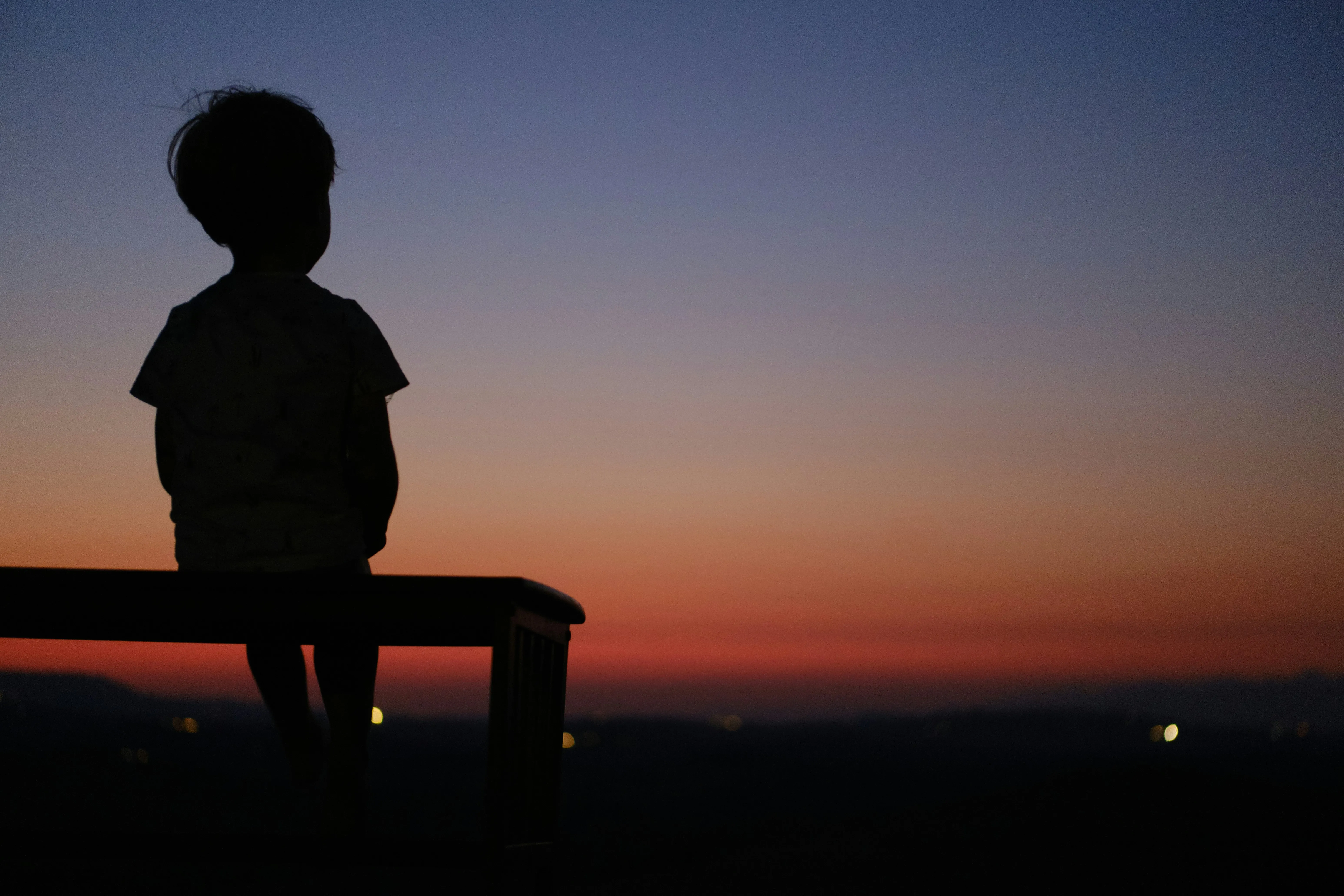A child in silhouette against a warm sunset sky, face turned away and unreadable.